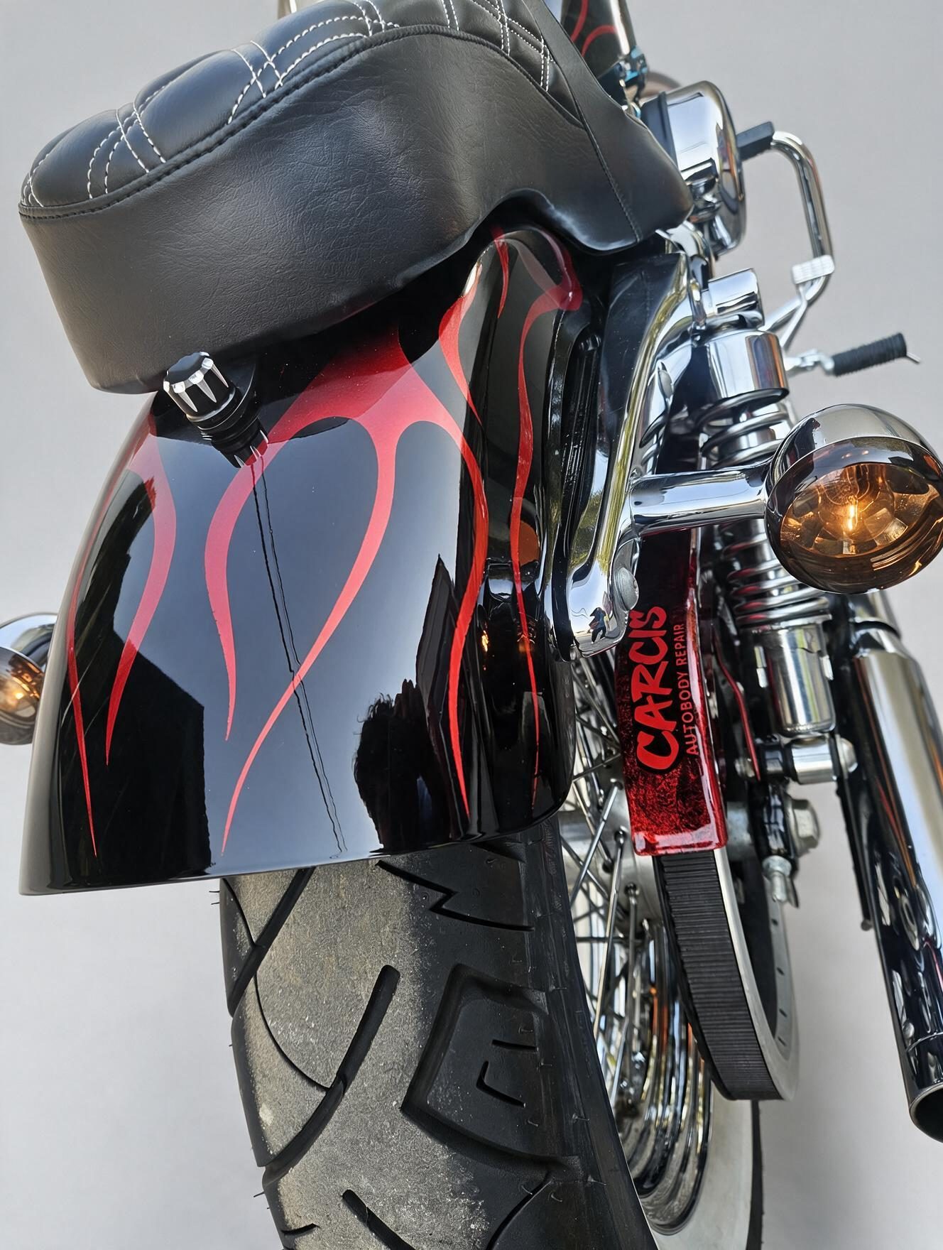 Close-up of a custom red flame paint job on a motorcycle rear fender, with a Carcis Autobody Repair license plate frame