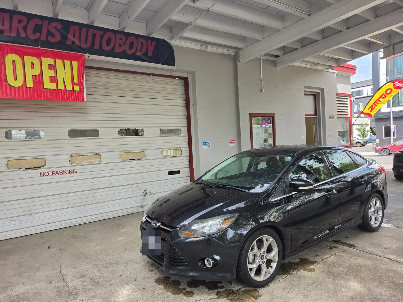 Front three-quarter view of the black 2014 Ford Focus parked outside Carcis Autobody Repair after dent repair.