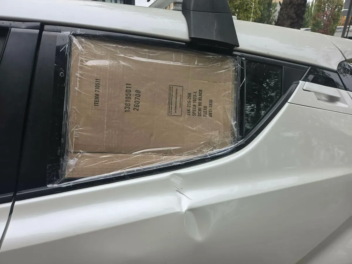 White Toyota C-HR rear passenger door showing crease dent and cardboard taped over missing window.