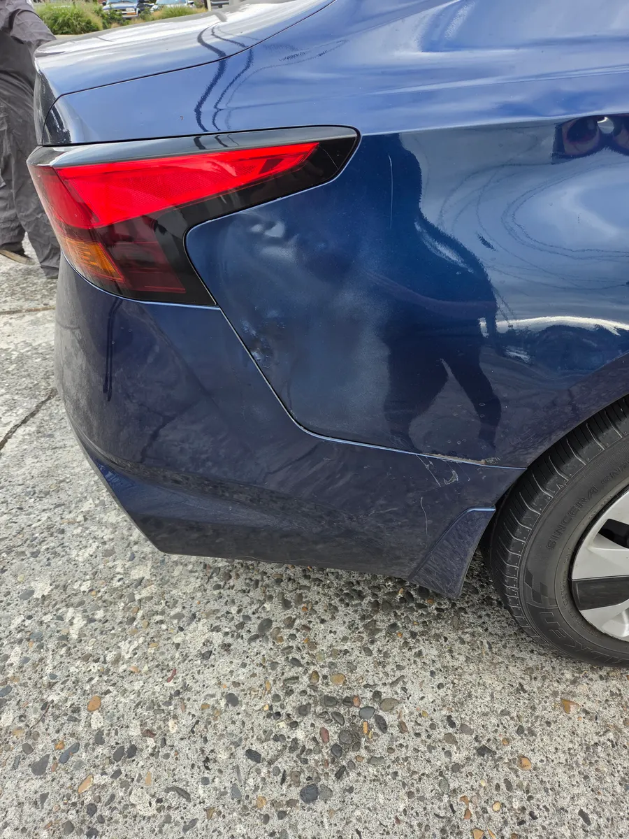 Rear quarter panel damage and tail light on a blue vehicle before repair.